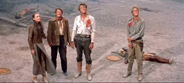 Four cowboys standing around a dirt ground, a scene from a western movie.